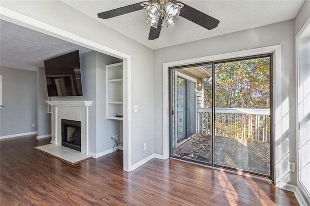 unfurnished living room featuring a fireplace, a textured ceiling, ceiling fan, and dark wood-type flooring