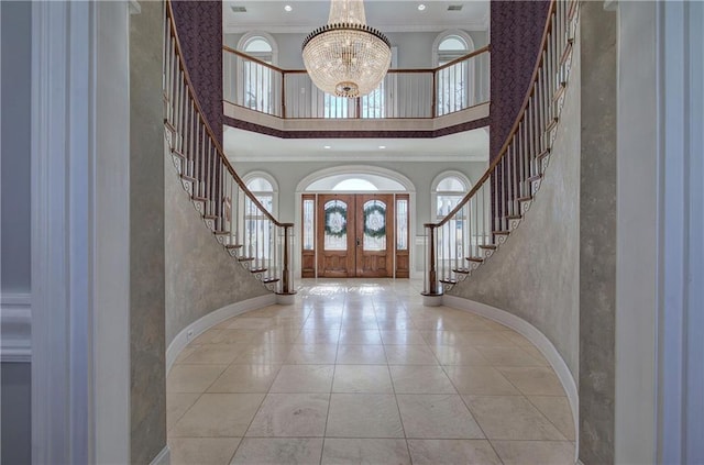 foyer with a chandelier, ornamental molding, a high ceiling, and french doors