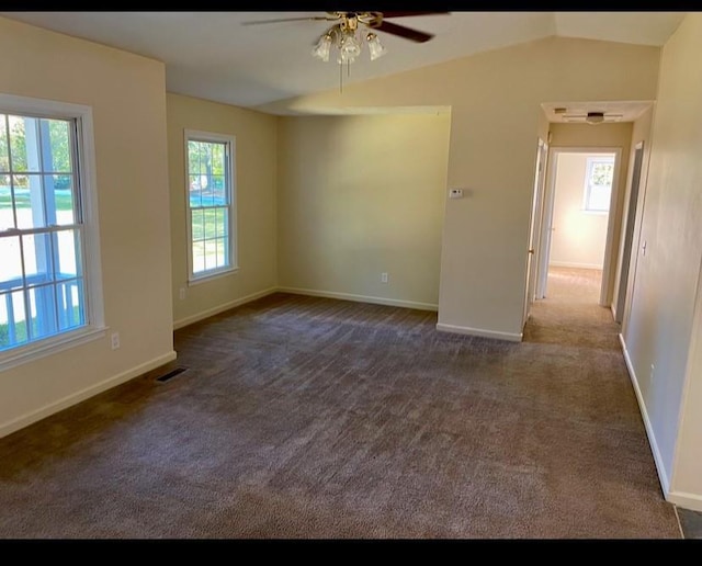 empty room with dark colored carpet, ceiling fan, lofted ceiling, and a wealth of natural light