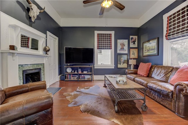 living area with a fireplace, wood finished floors, a ceiling fan, and baseboards