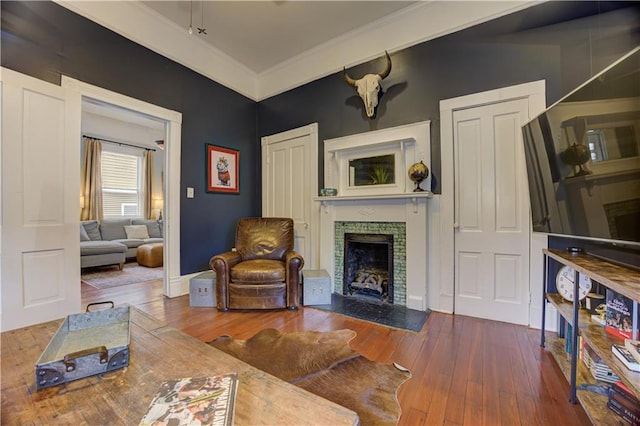 living room featuring a fireplace with flush hearth, crown molding, baseboards, and hardwood / wood-style flooring