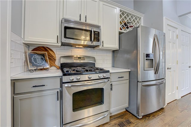 kitchen featuring stainless steel appliances, light countertops, backsplash, and wood finished floors