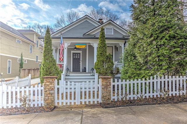 shotgun-style home with covered porch, a fenced front yard, and a chimney