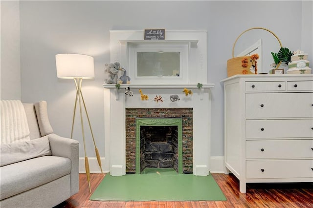 living area featuring a fireplace with flush hearth, wood finished floors, and baseboards