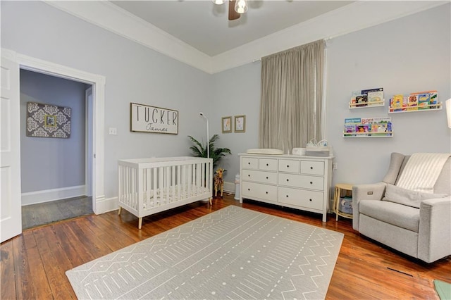 bedroom with a nursery area, wood-type flooring, baseboards, and ceiling fan