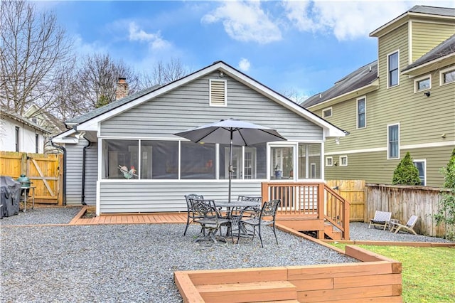 back of property featuring a chimney, a sunroom, a deck, and a gate