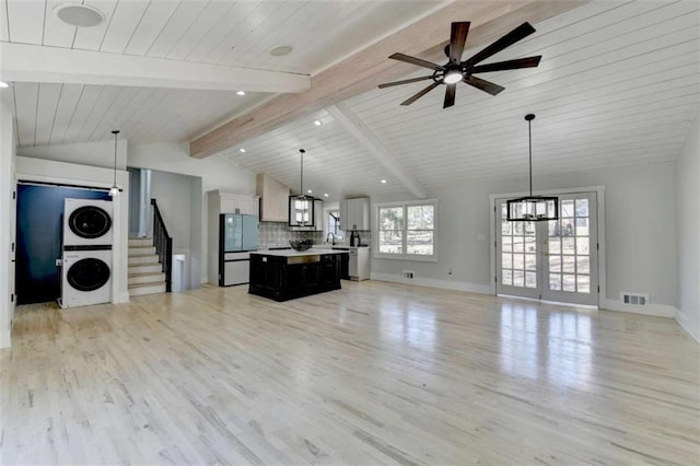 unfurnished living room featuring ceiling fan, vaulted ceiling with beams, stacked washer / drying machine, wooden ceiling, and light wood-type flooring