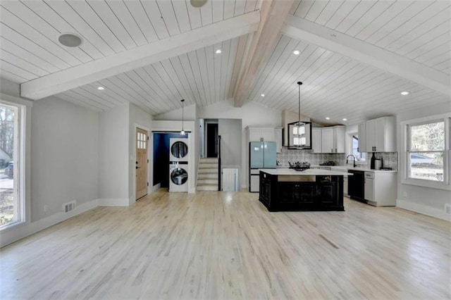 kitchen featuring stacked washer / drying machine, a center island, pendant lighting, decorative backsplash, and white cabinets