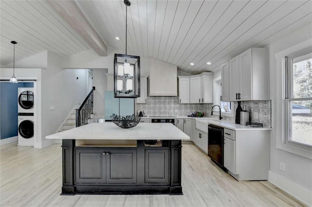 kitchen with dishwasher, white cabinetry, stacked washer / dryer, a kitchen island, and decorative light fixtures