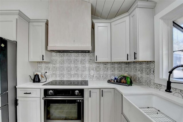 kitchen featuring sink, premium range hood, tasteful backsplash, black appliances, and white cabinets