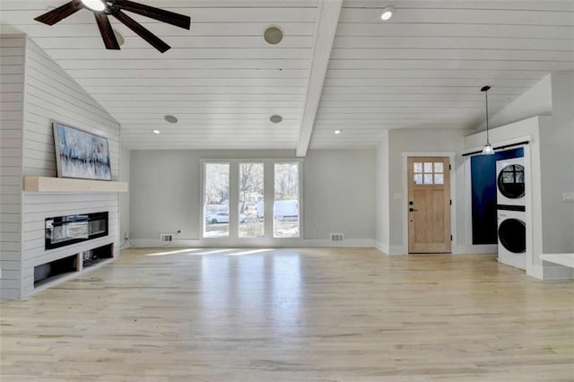 unfurnished living room with stacked washer / dryer, vaulted ceiling with beams, a fireplace, and light hardwood / wood-style floors