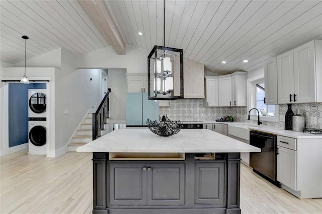 kitchen featuring stacked washer and dryer, white cabinetry, black dishwasher, and a center island