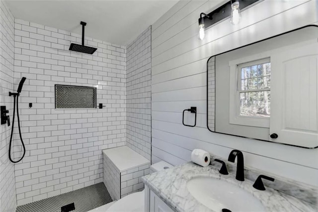 bathroom with a tile shower, vanity, wooden walls, and toilet