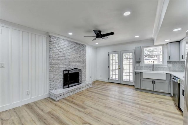 unfurnished living room featuring sink, ceiling fan, light hardwood / wood-style floors, a brick fireplace, and french doors