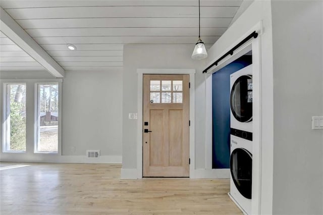 laundry area featuring stacked washer and dryer, a barn door, a wealth of natural light, and light wood-type flooring