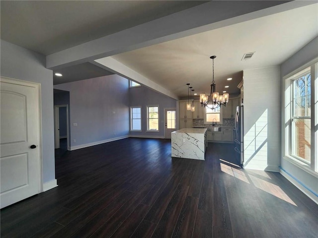 kitchen featuring backsplash, light stone countertops, hanging light fixtures, and cream cabinetry