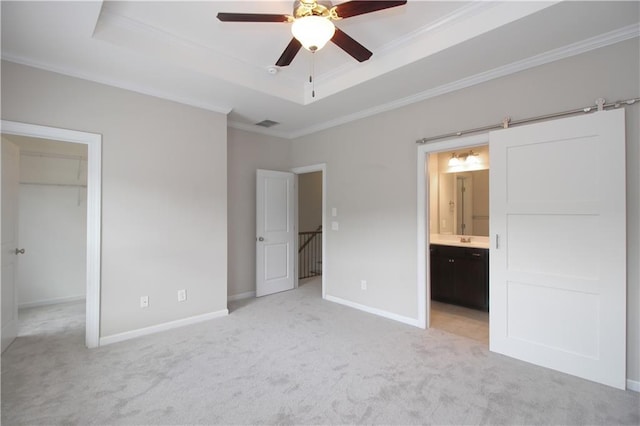 unfurnished bedroom featuring ornamental molding, light carpet, a raised ceiling, a spacious closet, and connected bathroom