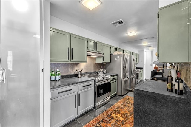 kitchen featuring green cabinetry, stainless steel appliances, dark countertops, tasteful backsplash, and under cabinet range hood