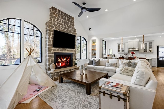 living room featuring high vaulted ceiling, light wood-style flooring, recessed lighting, a fireplace, and a ceiling fan