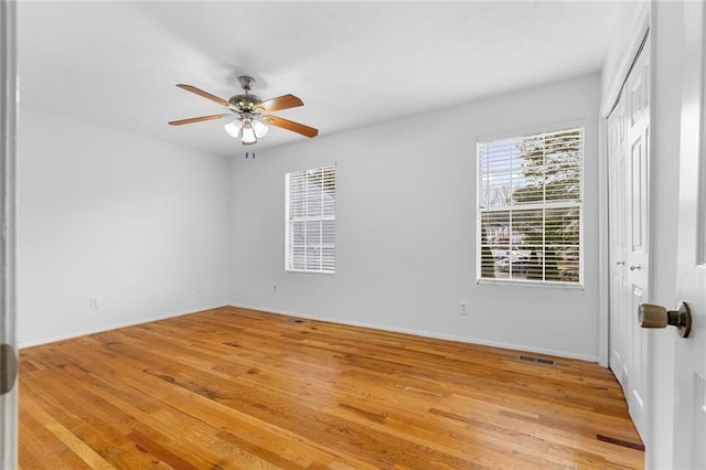 spare room with light wood-type flooring, ceiling fan, visible vents, and baseboards