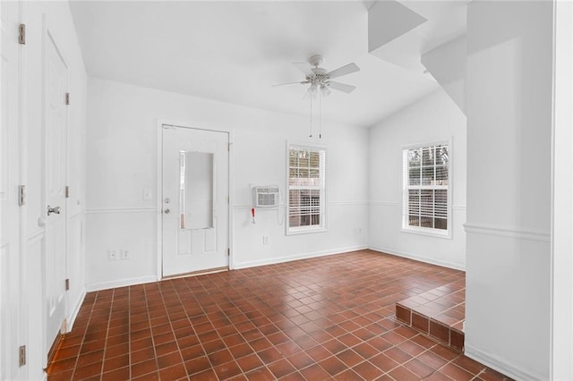 empty room featuring lofted ceiling, a wall unit AC, dark tile patterned flooring, a ceiling fan, and baseboards