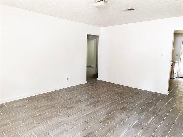 unfurnished room featuring dark wood-style floors, baseboards, visible vents, and a textured ceiling