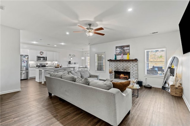 living area with visible vents, dark wood-style floors, a fireplace, and ceiling fan