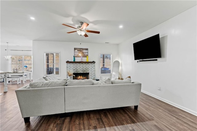 living area featuring a healthy amount of sunlight, ceiling fan, dark wood-type flooring, and a brick fireplace
