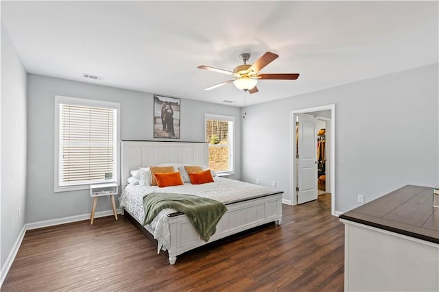 bedroom featuring dark wood-style floors, a spacious closet, baseboards, and a ceiling fan