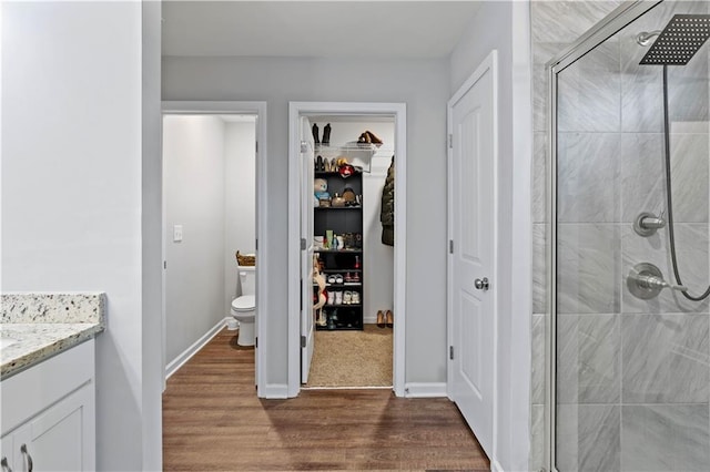 full bath featuring a shower stall, wood finished floors, toilet, vanity, and a spacious closet