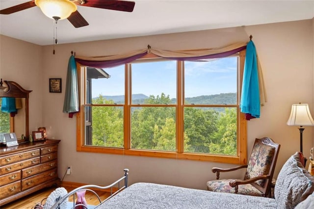 bedroom with a mountain view, a ceiling fan, multiple windows, and wood finished floors