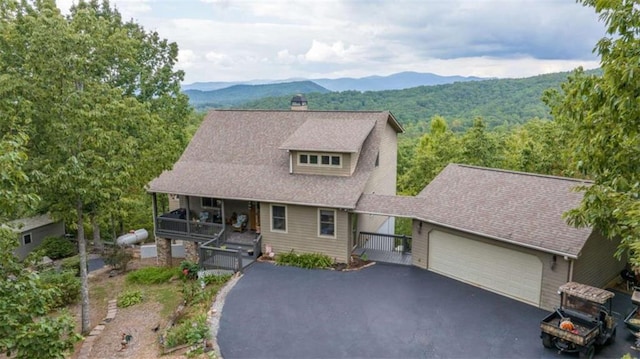view of front of house with a garage, a chimney, a mountain view, driveway, and roof with shingles