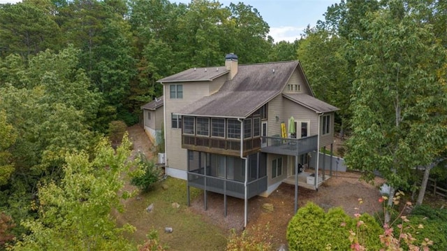 back of house featuring a chimney, a wooden deck, a sunroom, and roof with shingles