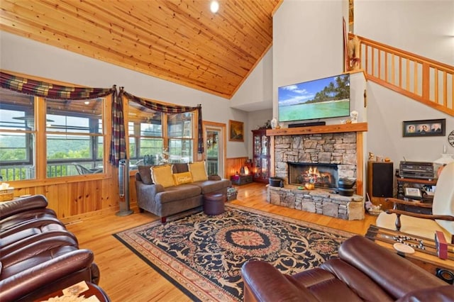 living area featuring wooden ceiling, high vaulted ceiling, a stone fireplace, wainscoting, and wood finished floors