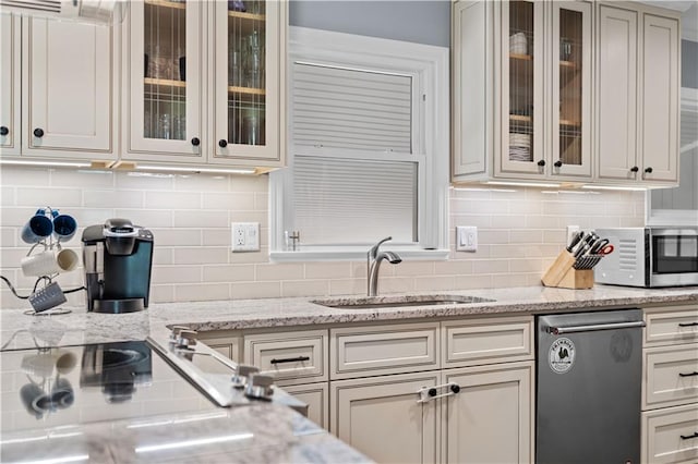 kitchen with tasteful backsplash, light stone countertops, appliances with stainless steel finishes, and sink