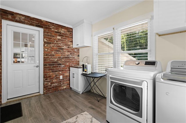 clothes washing area with ornamental molding, cabinets, dark wood-type flooring, washer and dryer, and brick wall