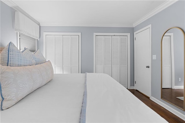 bedroom with dark hardwood / wood-style floors, crown molding, and two closets