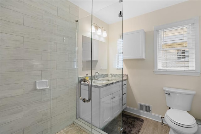 bathroom with hardwood / wood-style flooring, a shower with door, vanity, and toilet