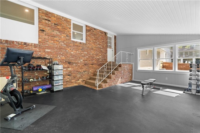 workout room featuring brick wall and lofted ceiling