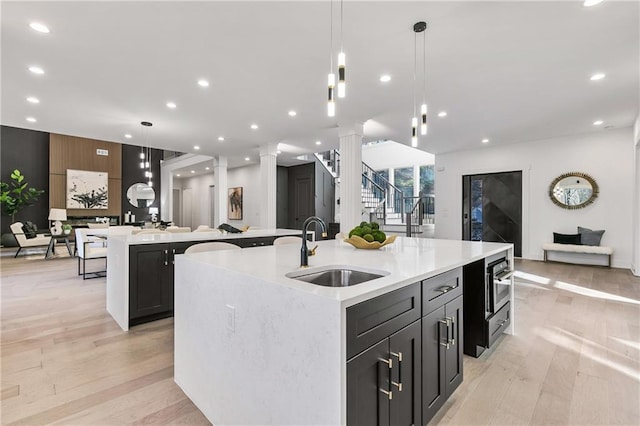 kitchen with open floor plan, decorative columns, a sink, and a large island with sink