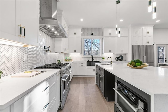 kitchen with pendant lighting, light countertops, appliances with stainless steel finishes, an island with sink, and wall chimney exhaust hood