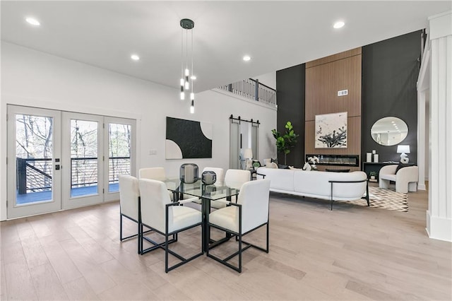 dining space featuring light wood finished floors, a barn door, a high ceiling, and recessed lighting