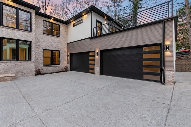 exterior space with a balcony, a garage, concrete driveway, and brick siding