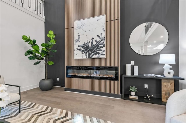 sitting room with a towering ceiling, an accent wall, a glass covered fireplace, wood finished floors, and baseboards