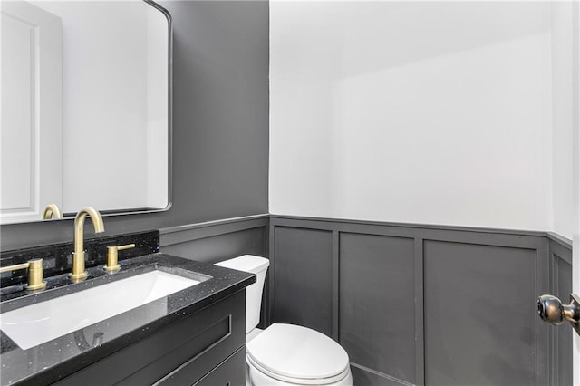 half bath with wainscoting, vanity, and toilet