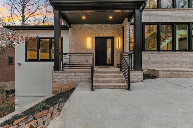 exterior entry at dusk featuring a porch and brick siding