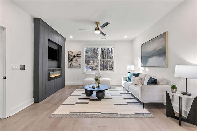 living area with light wood-style floors, a fireplace, baseboards, and a ceiling fan