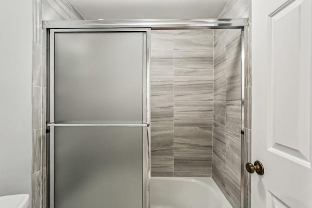 bathroom featuring shower / bath combination with glass door and toilet