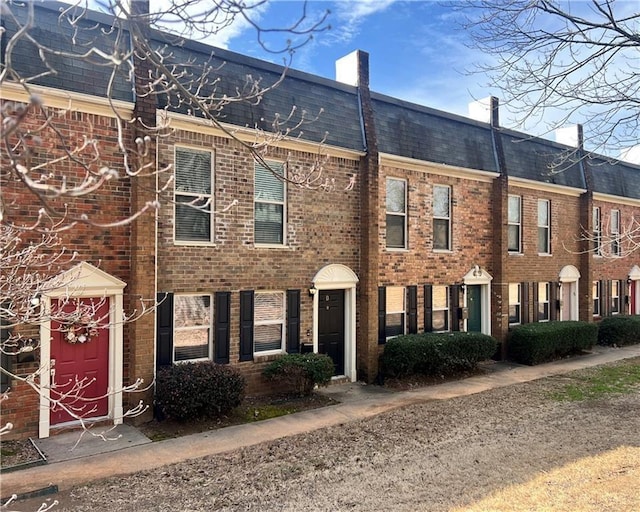 view of front of home with roof with shingles, a chimney, and brick siding