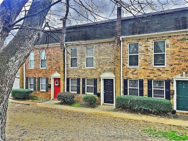 view of property with a shingled roof, a chimney, and brick siding